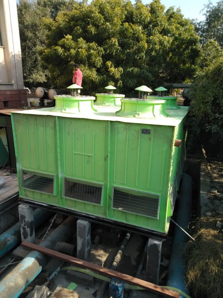 Four cell green FRP cooling tower on a concrete plinth with a technician on the fan deck
