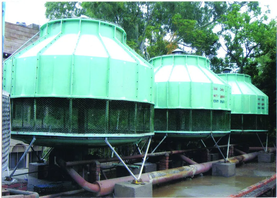 Three green round FRP cooling towers in a row on steel stands with common header pipework