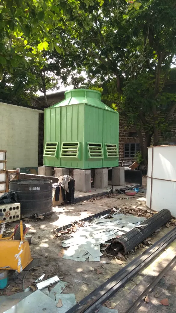 Green square FRP cooling tower installed on concrete pedestals beside a brick building