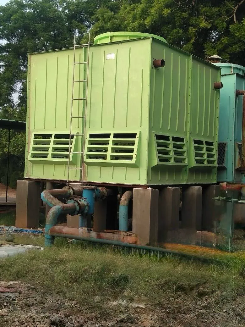 Green FRP cooling tower on concrete pedestals with blue header pipework